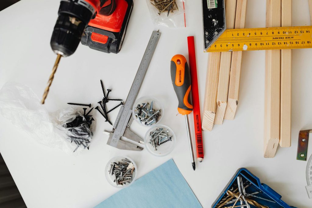 A collection of carpentry tools including drill, caliper, and try square on a white table.