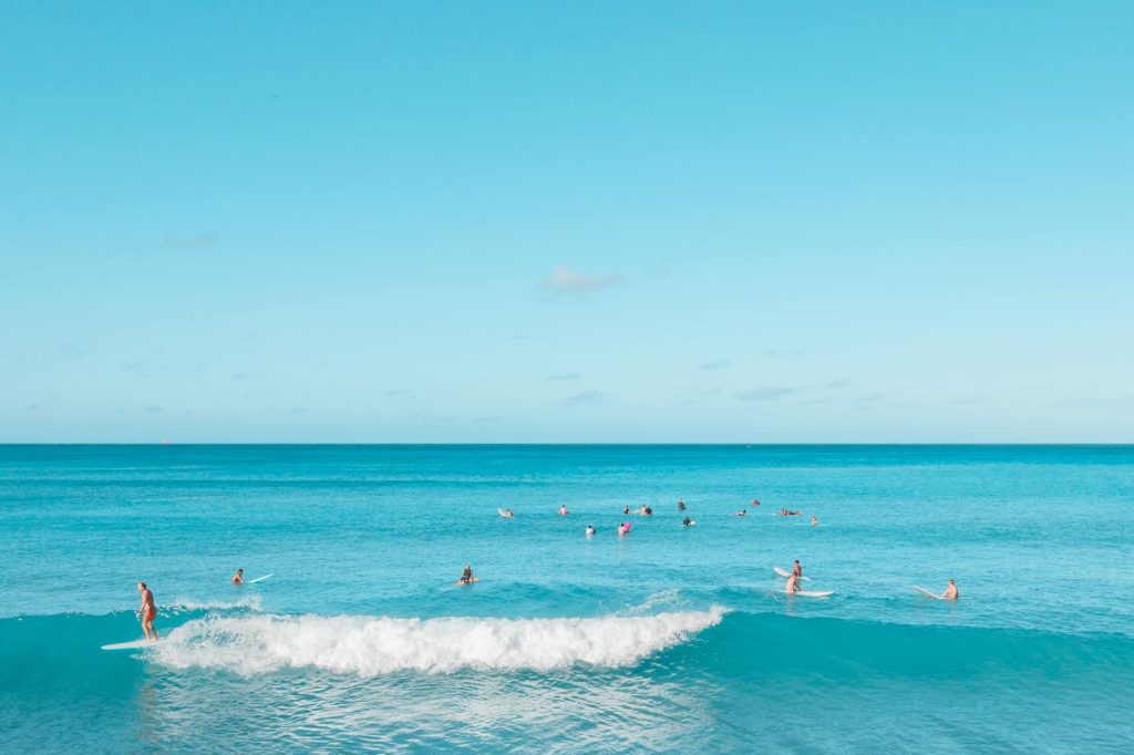 A lively scene of surfers riding turquoise waves under a clear summer sky.