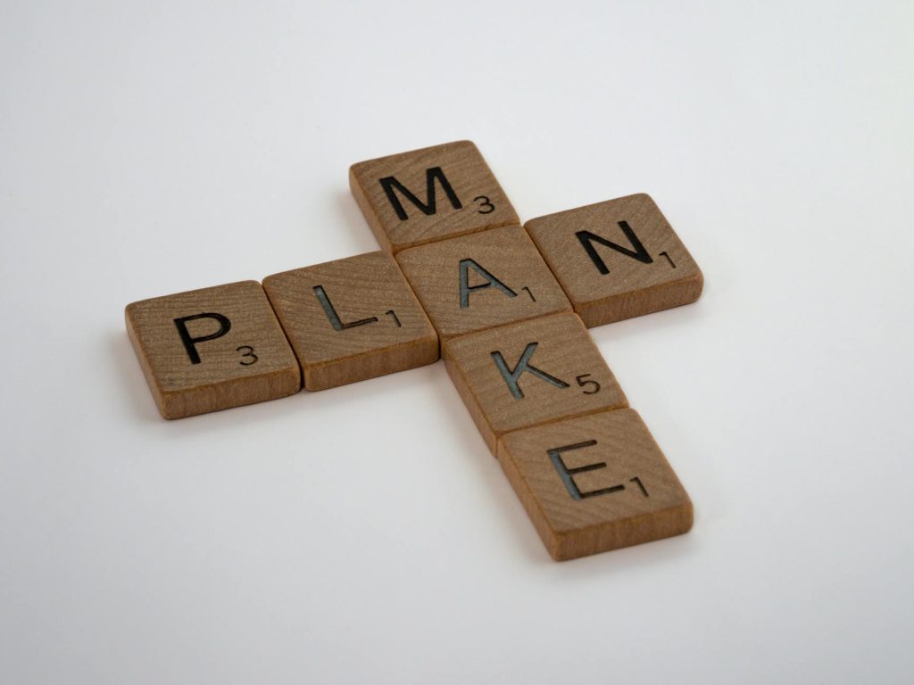 Wooden Scrabble tiles forming the words 'make' and 'plan' on a clean white background.