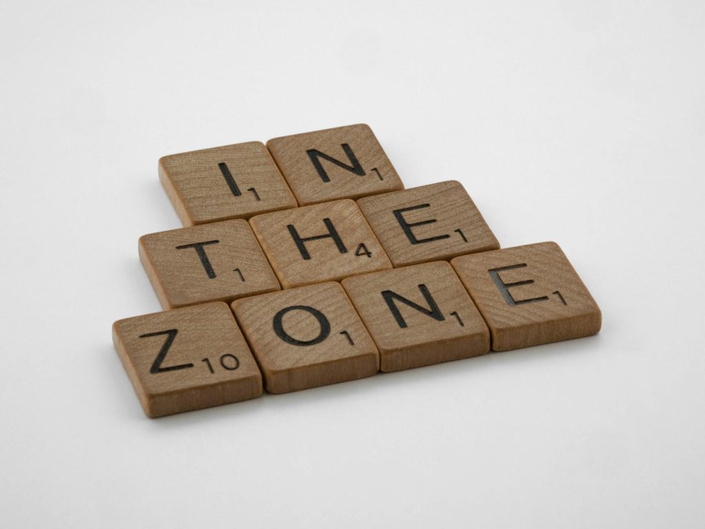 Scrabble tiles spelling out 'In the Zone' on a clean white background, symbolizing focus and concentration.