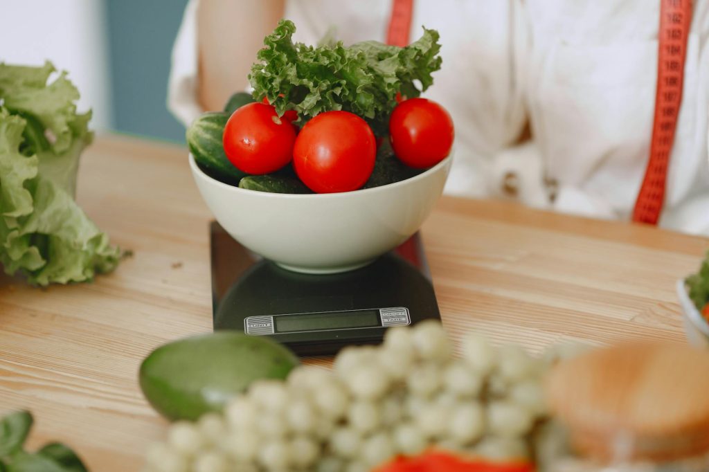 Colorful fresh vegetables including tomatoes and cucumbers on a kitchen scale for healthy eating.