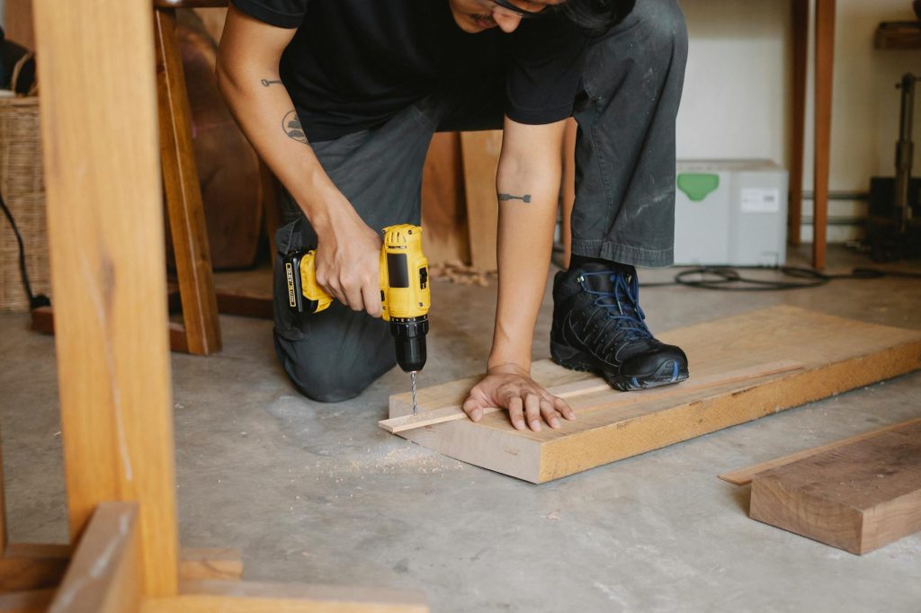 A focused craftsman using a drill to work on a wooden project in a workshop setting.