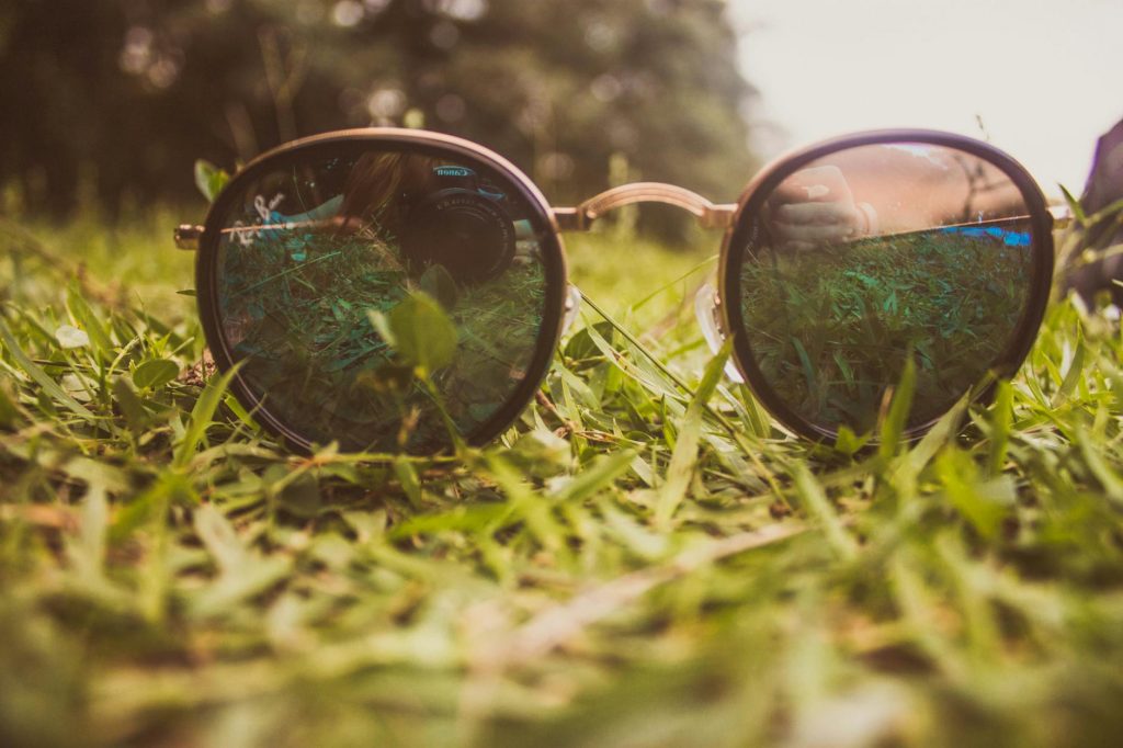 Close-up of sunglasses on grass reflecting nature and sky, emphasizing outdoor relaxation.