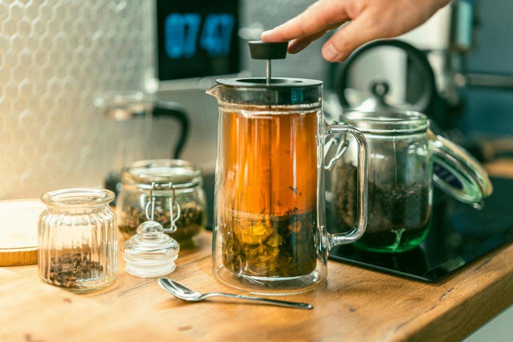 Hand brewing green tea with glass kettle and jars on wooden countertop in cozy kitchen.